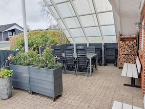 An outdoor patio with a covered seating area, planters with flowers, and a stack of firewood. - "Amila" - 500m to the fjord by Interhome (Roslev)