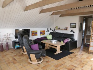 Ein Wohnzimmer mit einer schwarzen Ledersofa, zwei Ledersesseln, einem Holztisch und einem Fernseher.