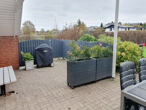 Eine Terrasse mit Grill, Pflanzkübeln und Gartenmöbeln.