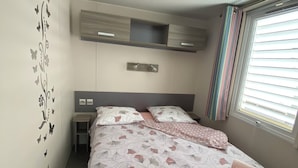 Une chambre à coucher comprenant un lit, une table de chevet, une étagère fixée au mur, une fenêtre avec des stores et un motif décoratif sur le mur.
