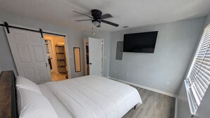 A bedroom with a bed, a ceiling fan, a TV mounted on the wall, and a window with blinds. - The Navarre Nook at The Spires - Near Navarre Beach & Pier (Navarre)