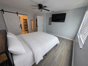 Ein Schlafzimmer mit einem Bett, einem Deckenventilator, einem an der Wand befestigten Fernseher und einem Fenster mit Jalousien.