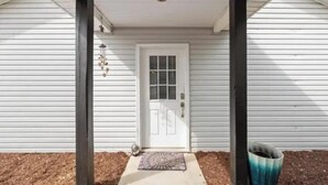 A white house with a front door, a porch, and a small garden area. - The Navarre Nook at The Spires - Near Navarre Beach & Pier (Navarre)