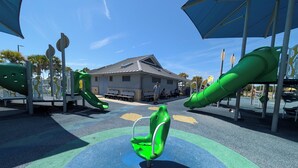 A playground with slides and benches, a building in the background, and a clear sky. - The Navarre Nook at The Spires - Near Navarre Beach & Pier (Navarre)
