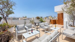 Eine Dachterrasse mit Sitzgelegenheiten im Freien, einem Tisch und einer Weinflasche.