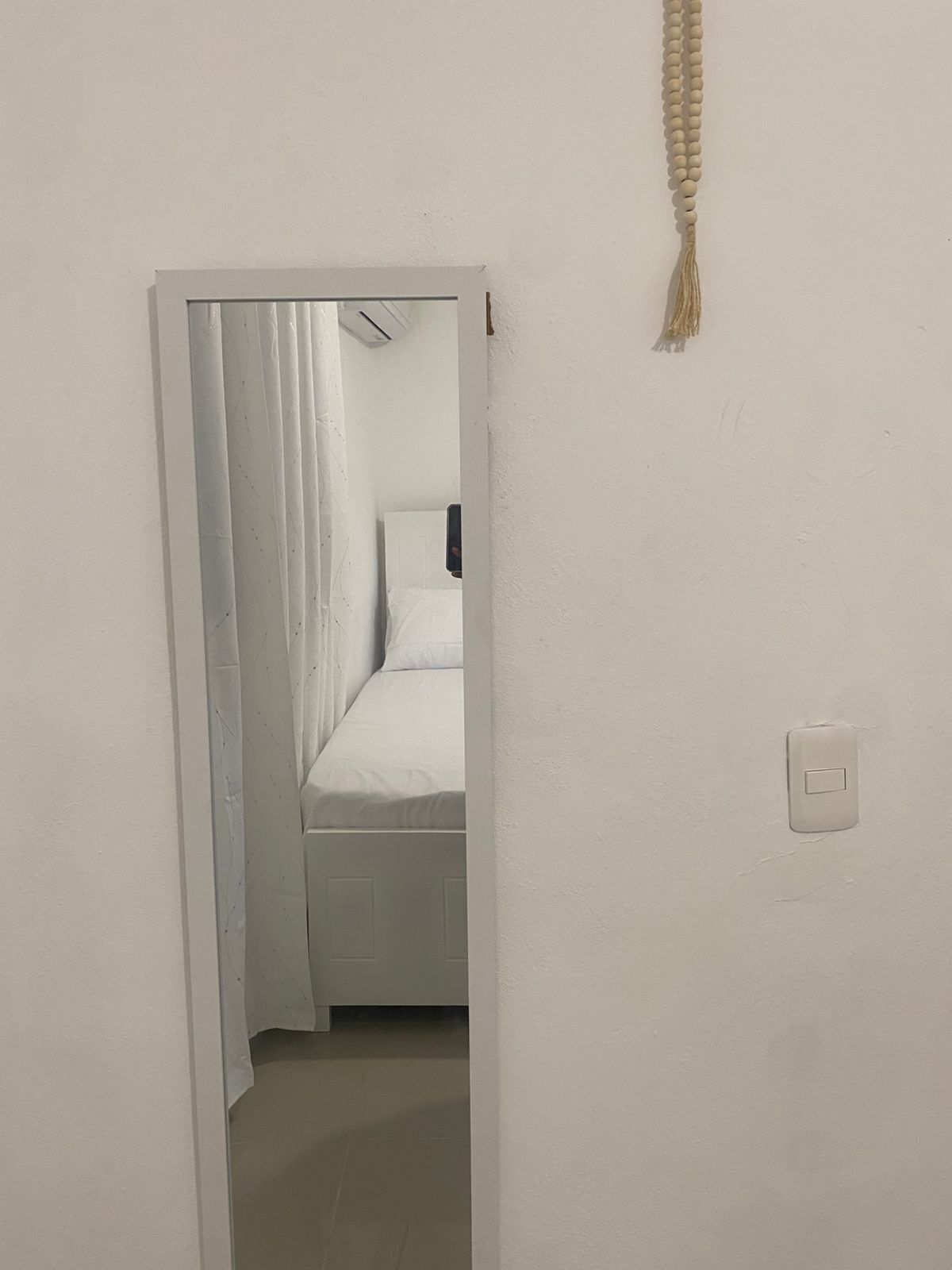 Een smalle gang die leidt naar een slaapkamer met een bed en een lichtschakelaar aan de muur.