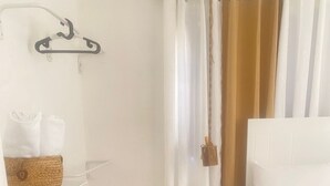 Een slaapkamer met een bed, een nachtkastje, een mand op een plank en een bezem die hangt.