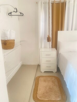 A bedroom with a bed, a nightstand, a basket on a shelf, and a hanging broom.