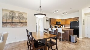 A modern kitchen with wooden cabinets, a black refrigerator, and a dining area with a wooden table and chairs. - Bright 3 Bd at Playa 548. Pool & Beach  (Kelowna)