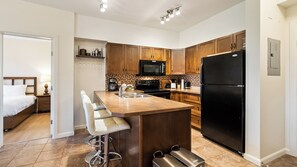 A modern kitchen with wooden cabinets, a black refrigerator, a microwave, and a bar stool. - Bright 3 Bd at Playa 548. Pool & Beach (Kelowna)