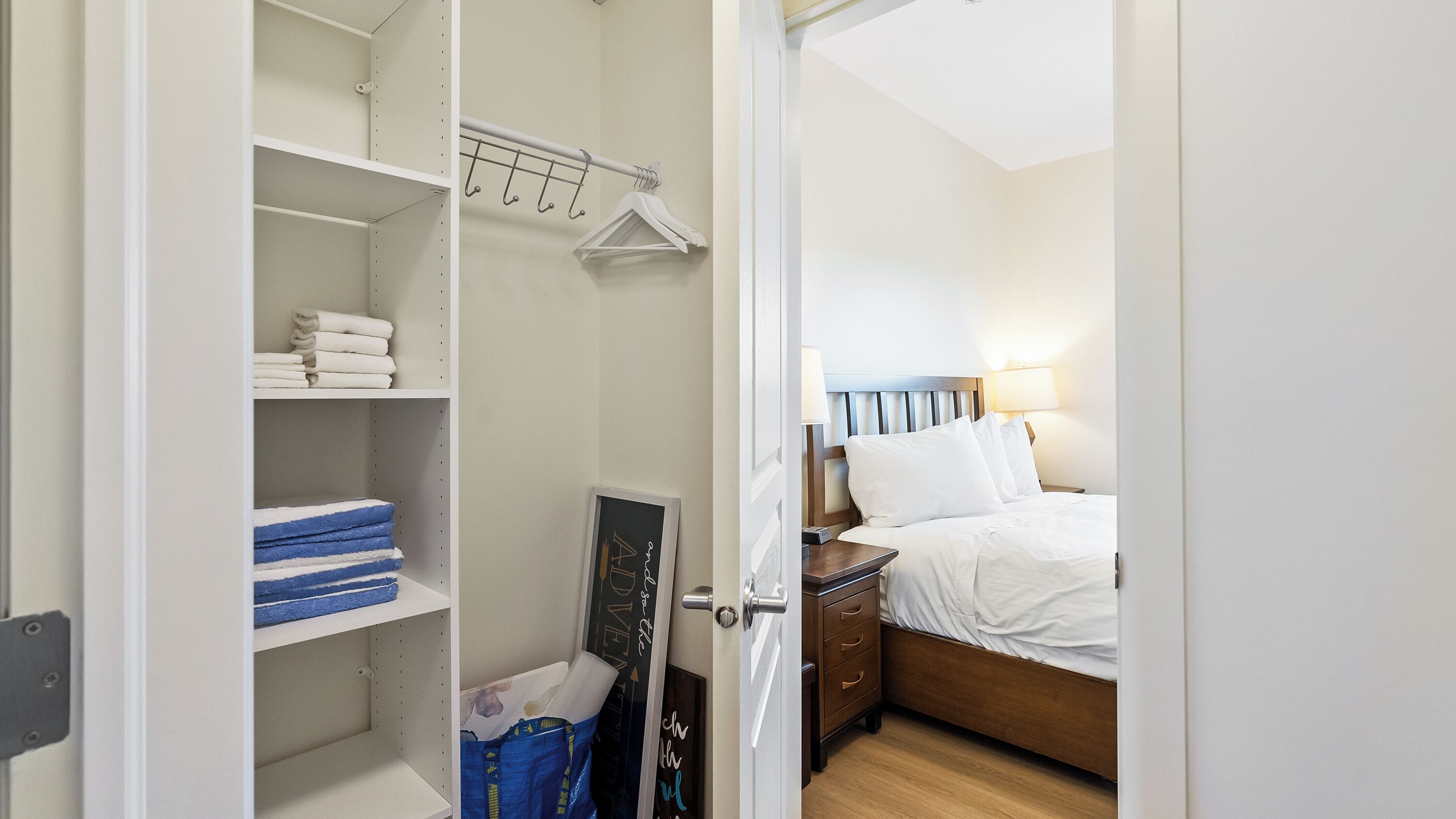 Ein Hotelzimmer mit Bett, Nachttisch, Kleiderschrank mit Regalen und Kleiderstange.