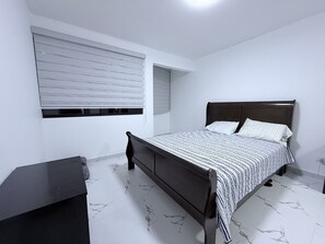 Ein Schlafzimmer mit Bett, Schreibtisch und einem Fenster mit Jalousien.