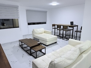 Ein modernes Wohnzimmer mit Sofa, Hocker, Couchtisch und Esstisch.