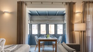 Ein Hotelzimmer mit einem Bett, einer Couch, einem Esstisch mit Stühlen und Blick ins Freie.