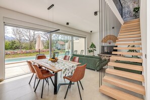 Un intérieur moderne comprenant un coin repas, un canapé vert, un escalier et une vue sur l’extérieur.