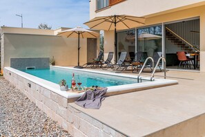 Piscina com espreguiçadeiras, mesa com bebidas e escadaria para uma área coberta.