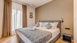 A bedroom with a large bed, curtains, a bedside table, and wall-mounted light.
