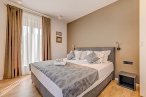 Un dormitorio con una cama grande, cortinas, una mesita de noche y una lámpara en la pared.