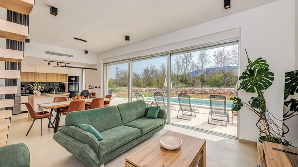 A modern living room with a green sofa, wooden coffee table, and a dining area with chairs.