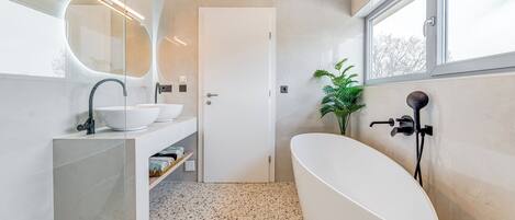 Un bagno moderno con una vasca da bagno freestanding, uno specchio grande e una finestra che lascia entrare luce naturale.