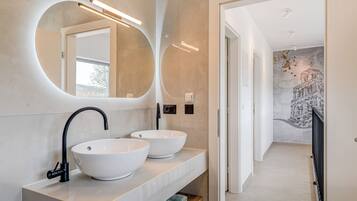 A modern bathroom with two white vessel sinks, a large mirror, and a light fixture.