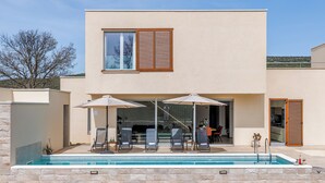 A modern two-story house with a swimming pool, outdoor seating, and a patio area.