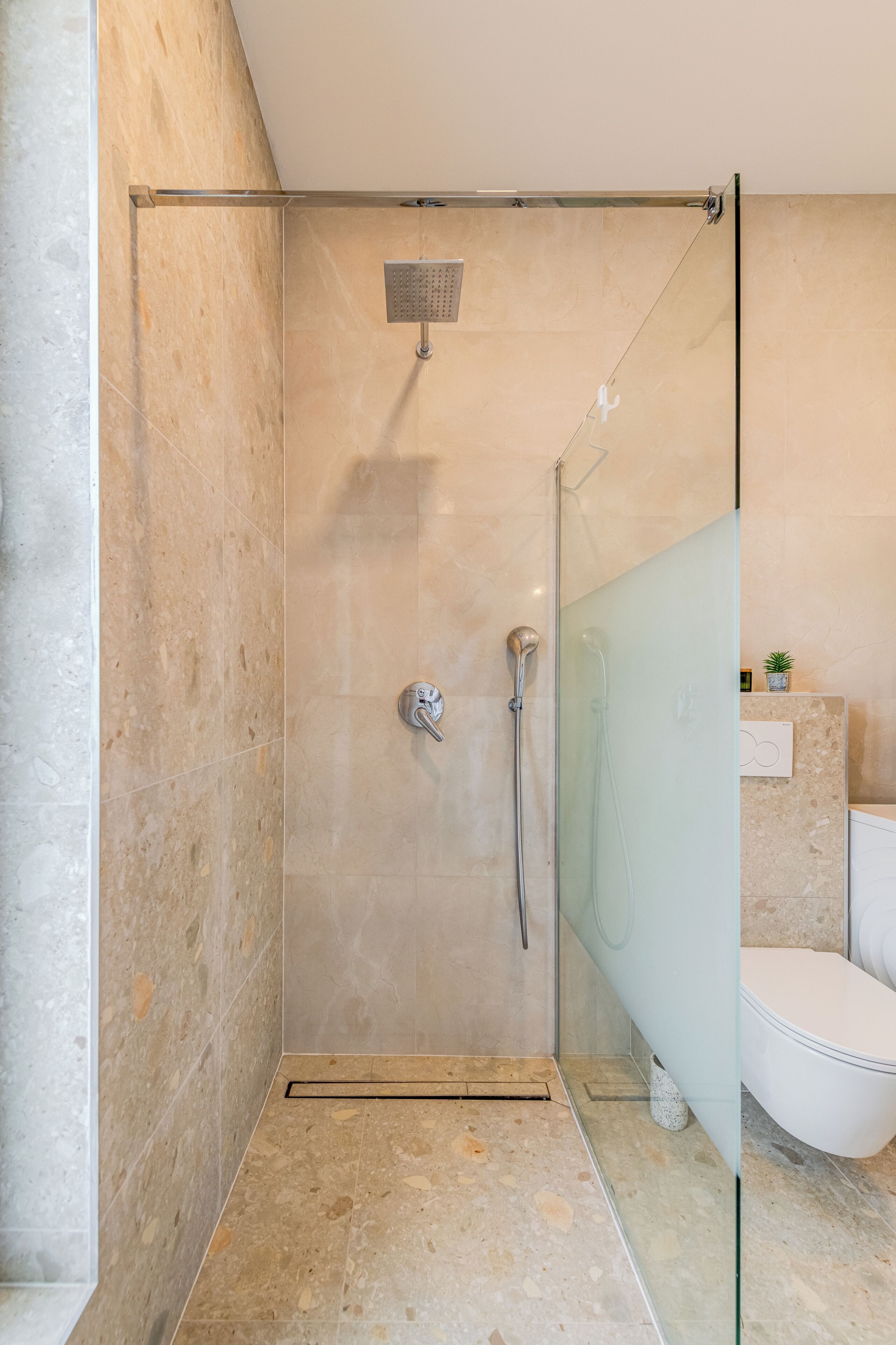 A modern bathroom with a glass-enclosed shower, a white toilet, and a marble floor.