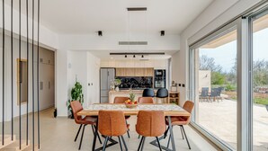 A modern kitchen with a central island, a dining area with a table and chairs, and a large sliding glass door leading to an outdoor patio.