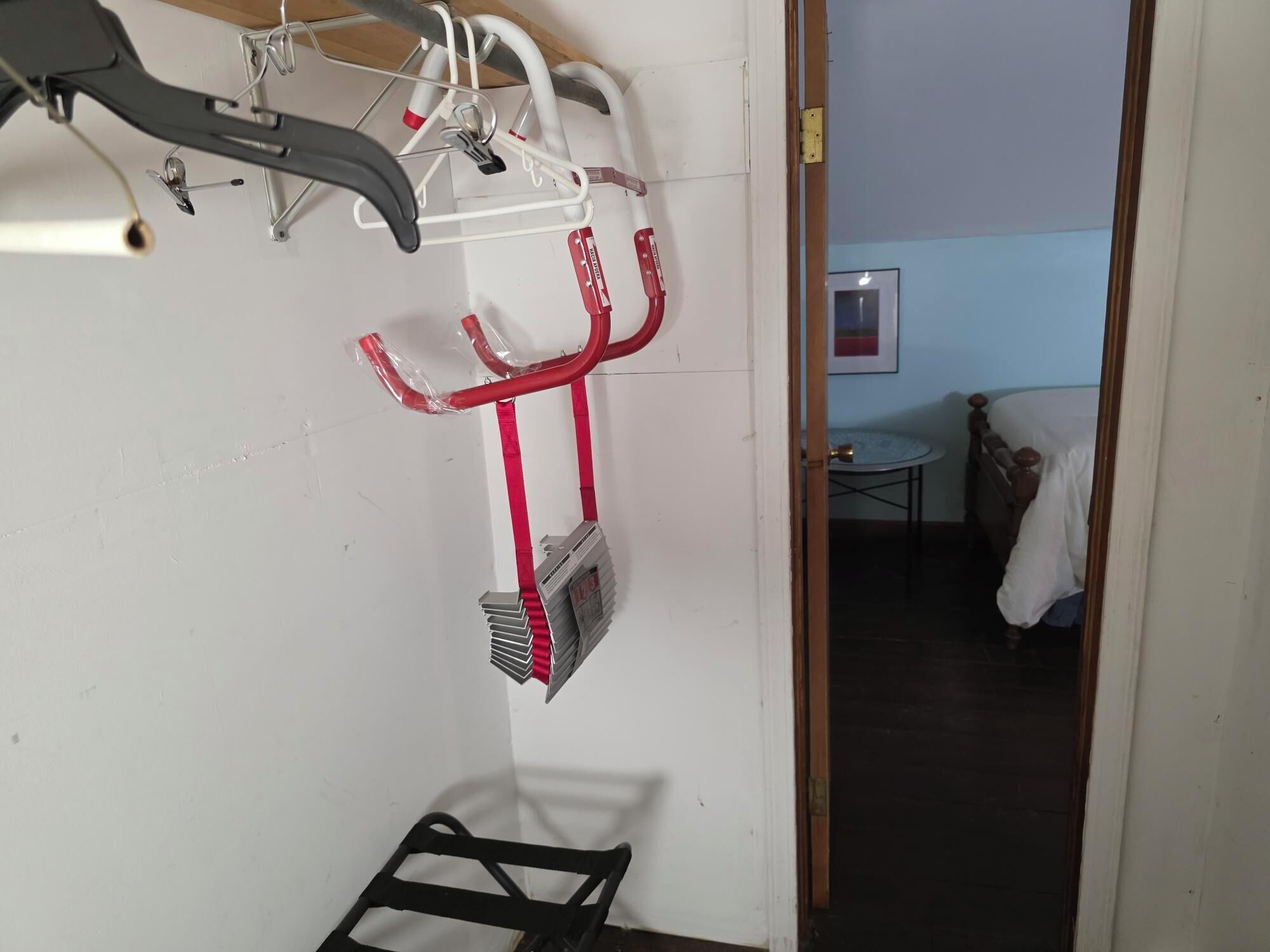 Ein Zimmer mit einem Bett, einem kleinen Tisch und einem an der Wand befestigten Ablagefach mit Gegenständen.