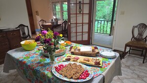 Uma mesa de jantar com toalha florida, diversos alimentos e um vaso de flores.
