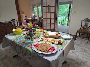 A dining table with a floral tablecloth, various food items, and a vase of flowers. - House in 3-acre woods, YMCA walkable, Hartwell 2 min, lake 10 min, Opal Retreat  (Hartwell)