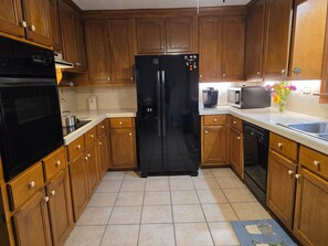 A kitchen with wooden cabinets, a black refrigerator, a coffee maker, and a microwave.