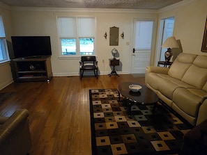 Una sala de estar con un sofá, una televisión, piso de madera y una alfombra estampada.