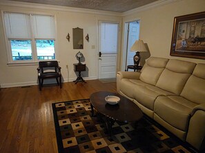 A living room with a beige sofa, a wooden coffee table, a patterned rug, a chair, a lamp, and a painting on the wall.