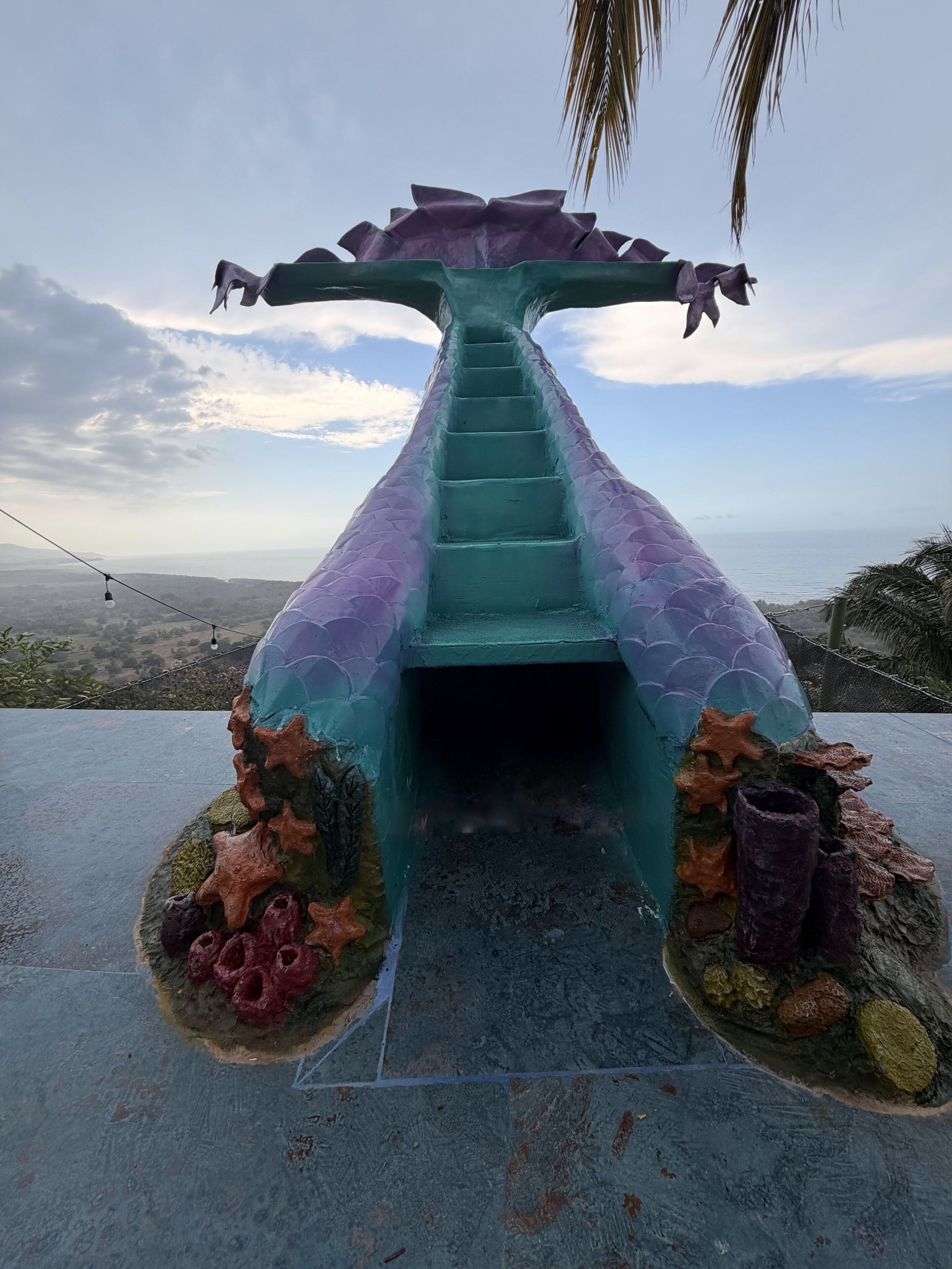 A staircase leading to a structure resembling a mermaid's tail, surrounded by artificial coral and starfish.