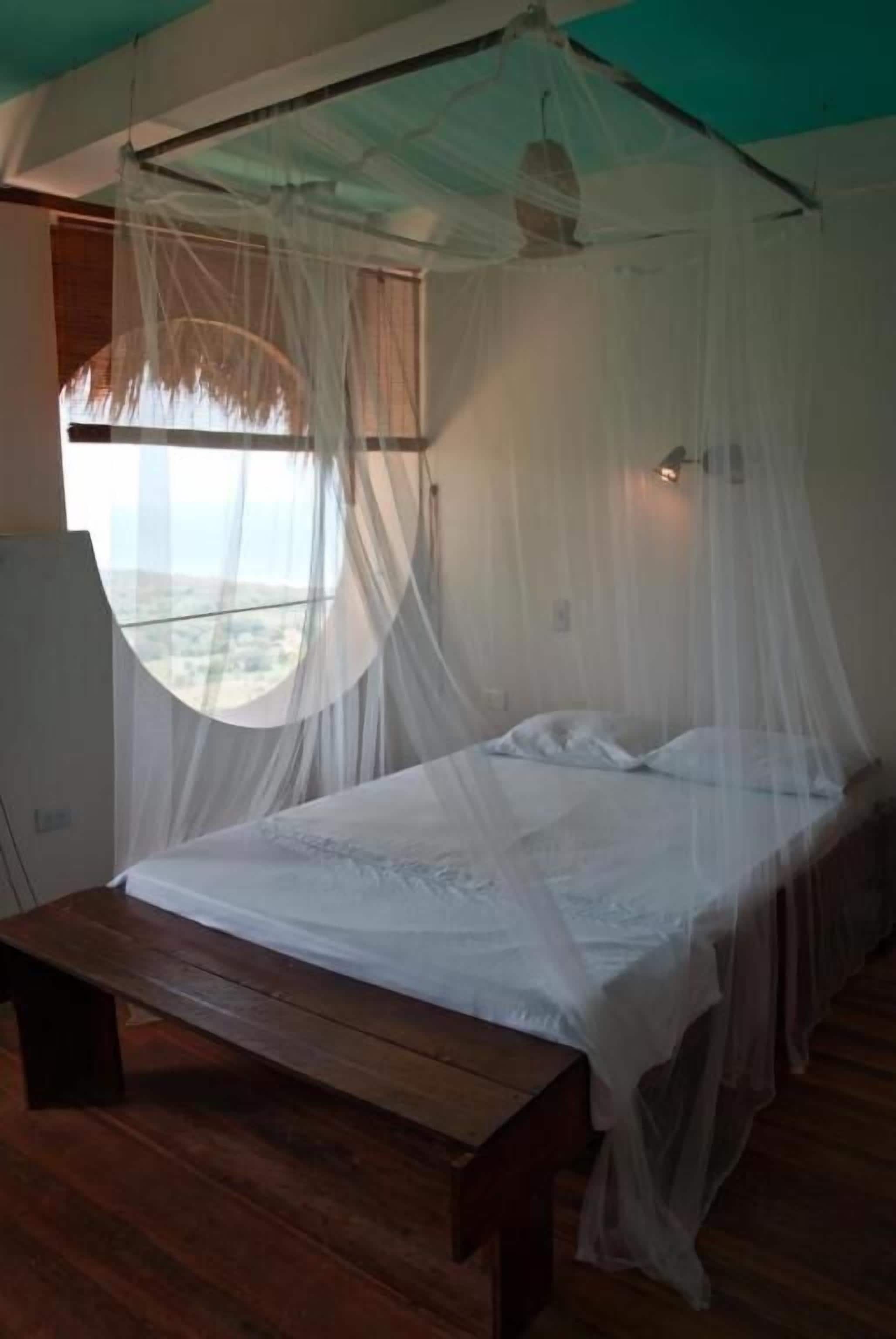 A bed with a canopy, a wooden bench, and a window with a view.