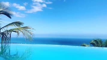 Cielo azul despejado, un océano tranquilo y una piscina con palmeras.