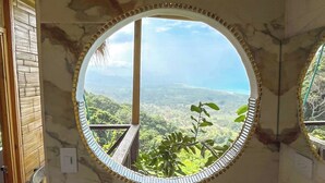 Casa de banho com espelho redondo, lavatório e vista para a paisagem.
