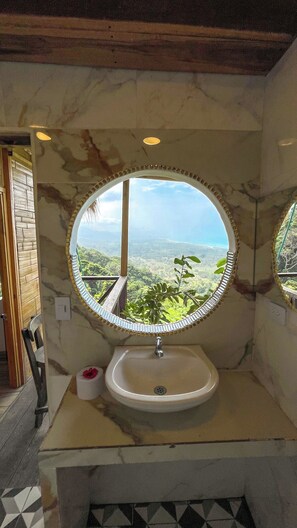 Ein Badezimmer mit rundem Spiegel, Waschbecken und Blick auf eine Landschaft.