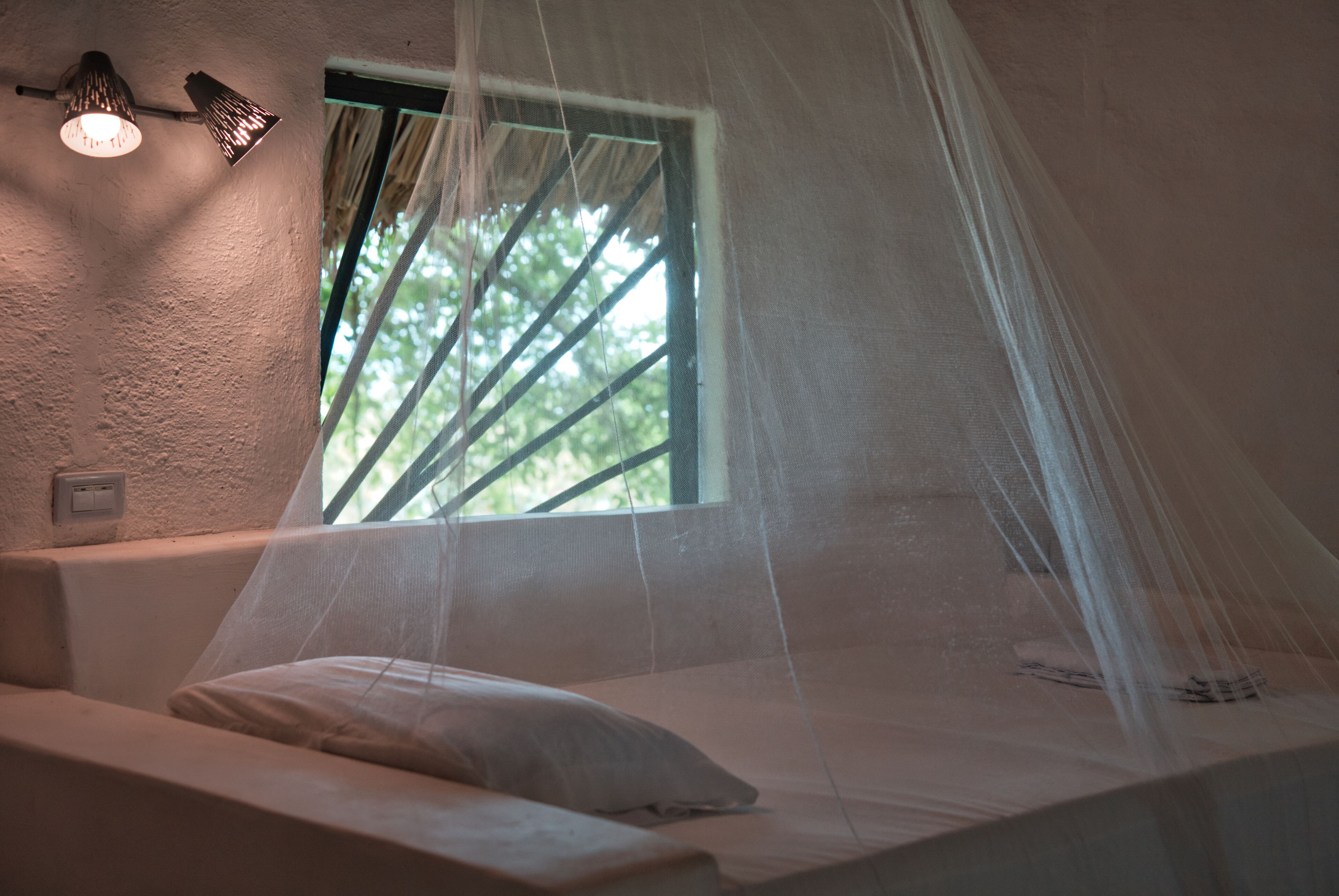Ein Zimmer mit einem Bett, einem Fenster mit Blick auf Bäume und einer Wandleuchte.