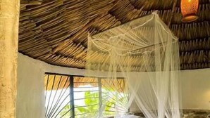 A bed with a canopy in a room with a thatched ceiling and stone walls.