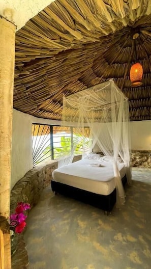 Una cama con dosel en una habitación con techo de paja y paredes de piedra.