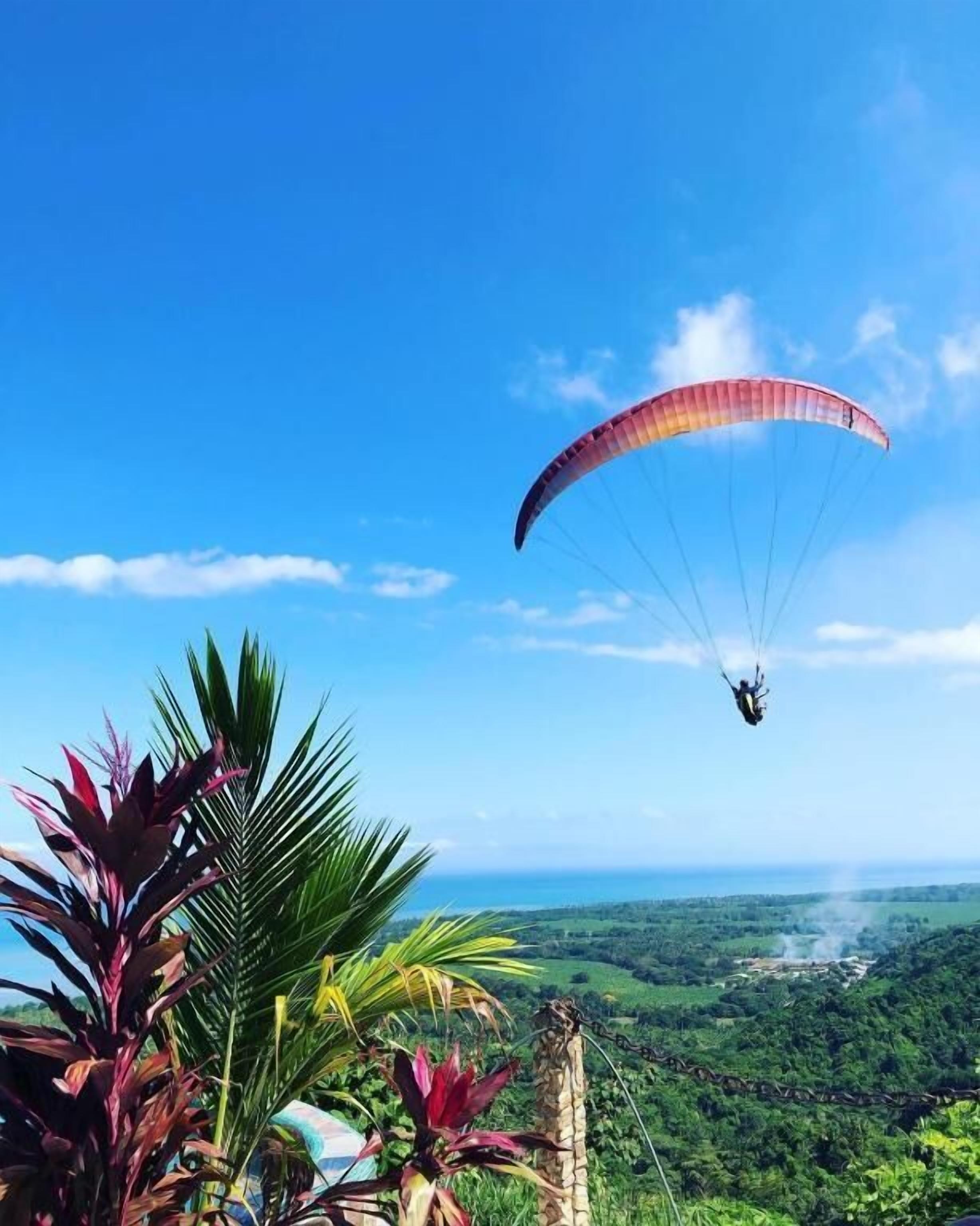 A paraglider in the air with a clear view of a lush landscape below.