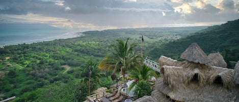 A thatched-roof structure with outdoor seating and a view of a coastal landscape.
