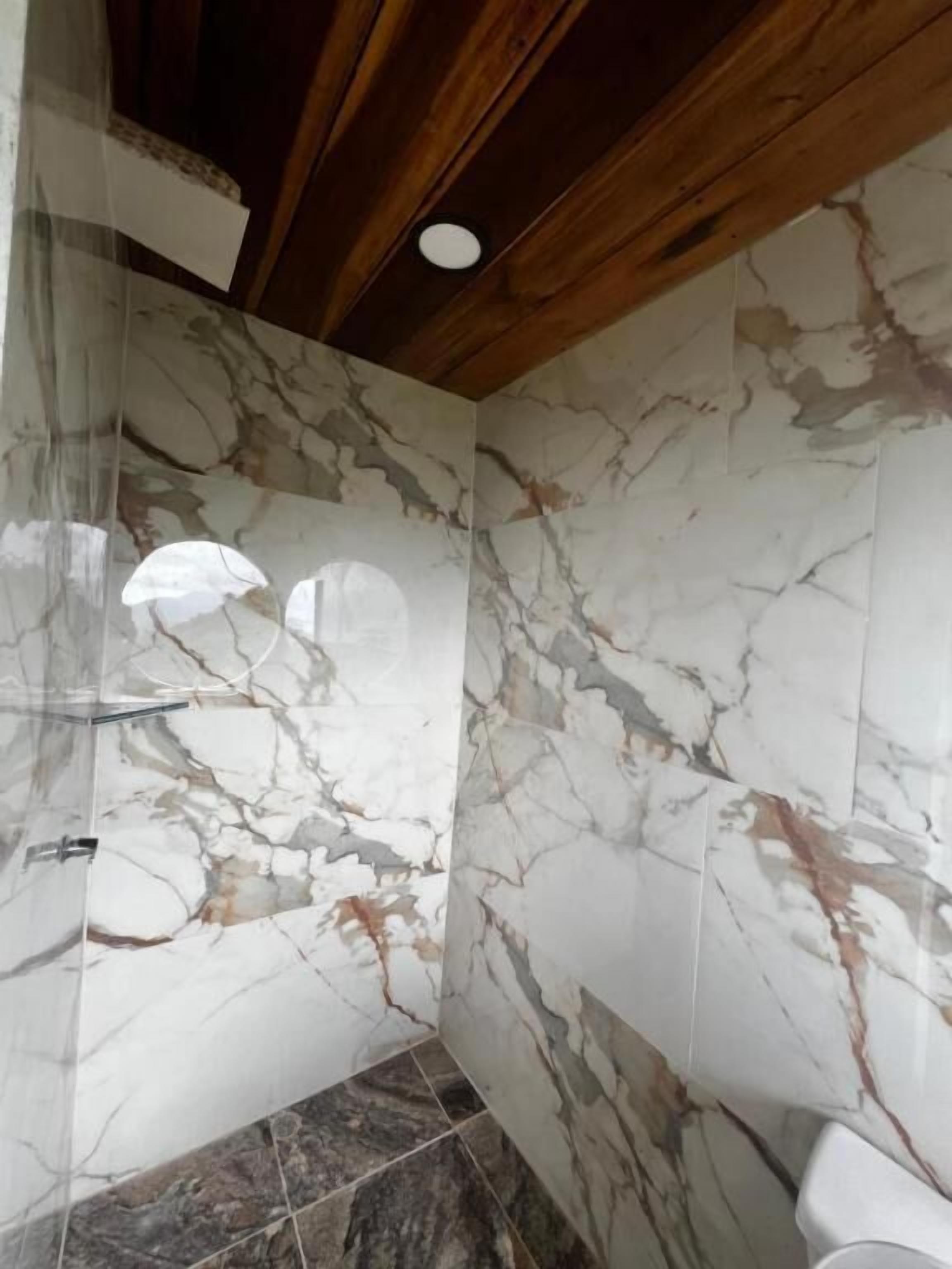 A bathroom with marble walls, a shower area, and a wooden ceiling.