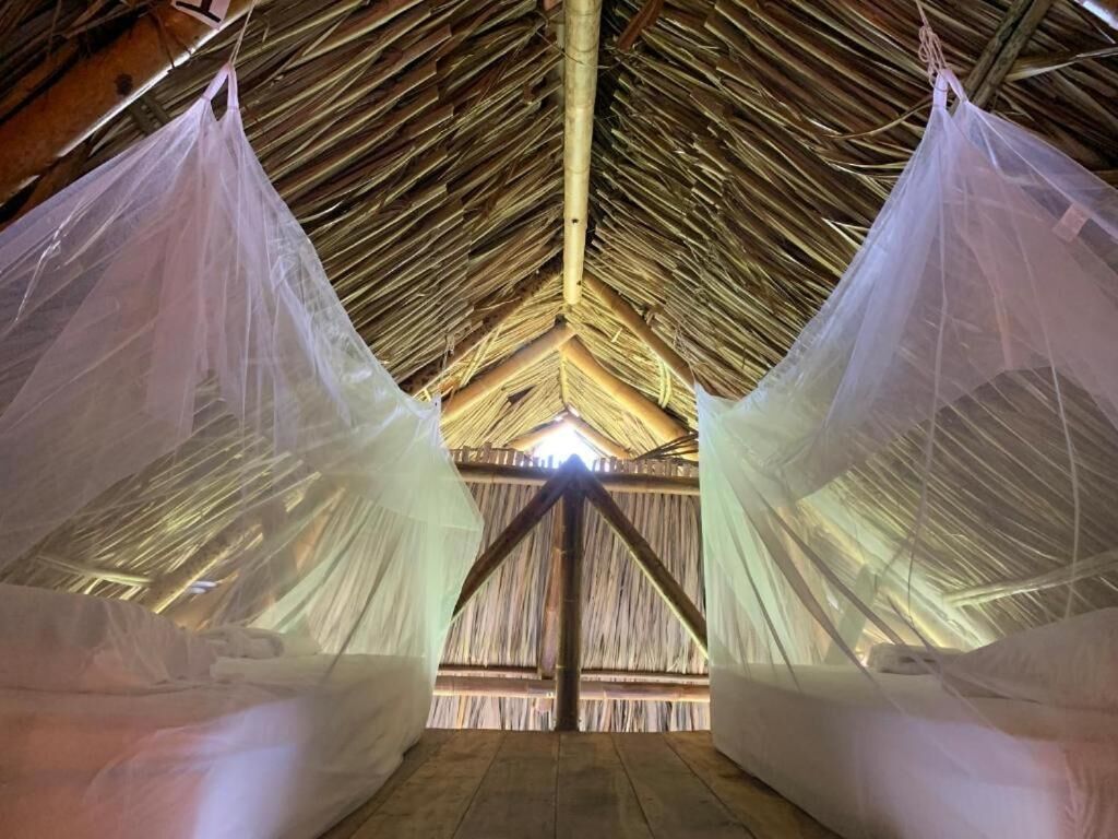 A thatched-roof structure with a central wooden beam and fabric drapes.