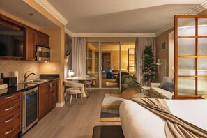 Ein Hotelzimmer mit Küchenzeile, Essbereich, Wohnzimmer mit Sofa und großem Fenster sowie eine Glastür, die auf einen Balkon führt.