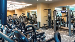 Ett gym med olika träningsmaskiner, en vägg med speglar och en tv-skärm.