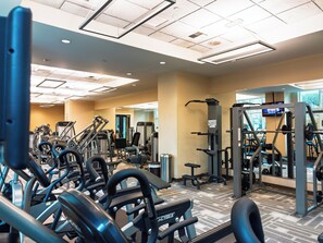 Ein Fitnessstudio mit verschiedenen Trainingsgeräten, einer Spiegelwand und einem Fernsehbildschirm.