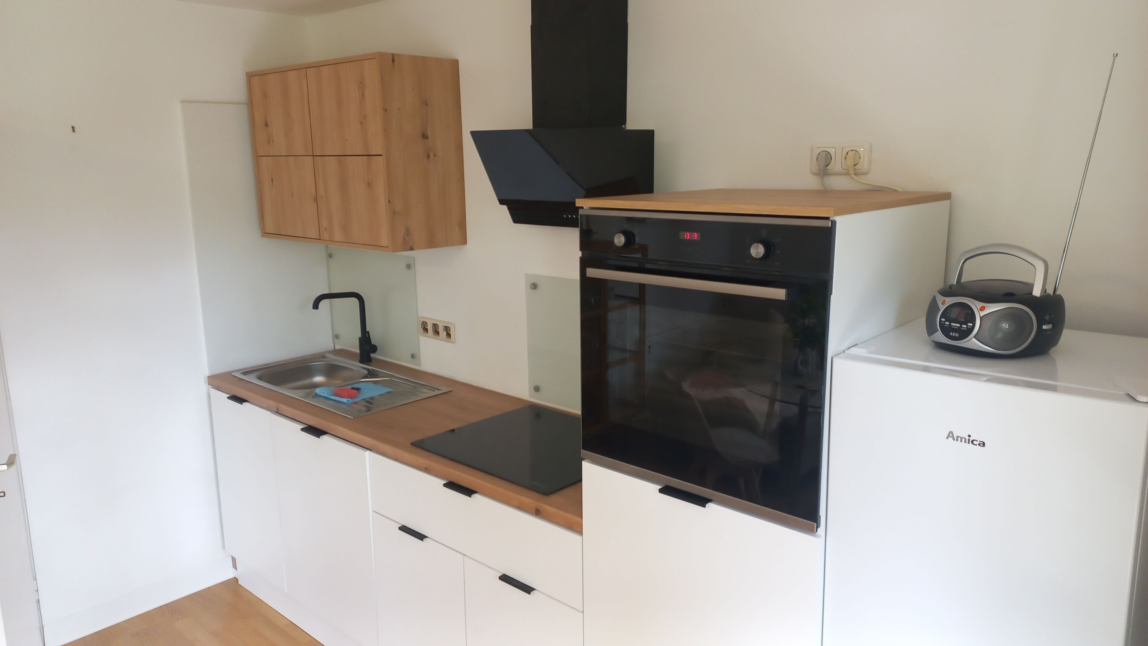 A compact kitchen with a sink, stove, and a radio on top of a white refrigerator.
